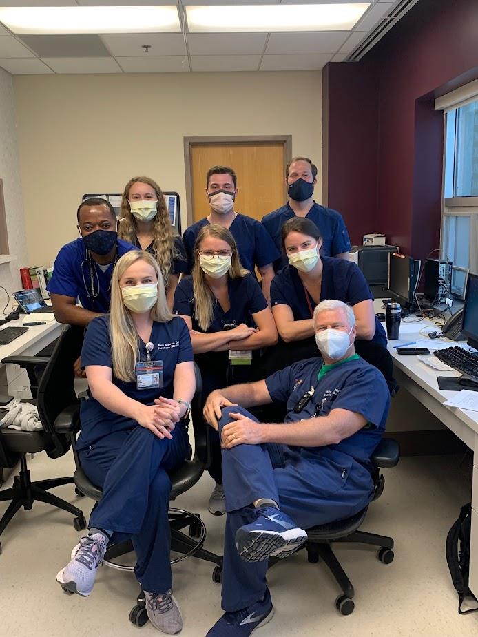 group picture of pediatric residents and faculty wearing surgical masks and blue scrubs in office setting